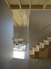 Modern home with Kitchen. Interior view from guest room to staircase and kitchen. The staircase is made of pine with a sliding rack attached to the catch. The roof with visible solid wood construction and walls of grey coloured wood fibreboards. The floor is glossy and dust-bound concrete floor. Photo 8 of Späckhuggaren