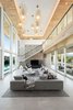 Modern home with Living Room, Sofa, Standard Layout Fireplace, Porcelain Tile Floor, Recessed Lighting, Ceiling Lighting, Accent Lighting, Coffee Tables, Gas Burning Fireplace, and Sectional. Floating stairs with glass railings wrap the fireplace, which is the feature piece of the soaring double-height living room. Photo 3 of BUILDER Chōwa Concept Home