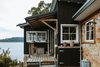 Modern home with Outdoor, Wood Fences, Wall, Decking Patio, Porch, Deck, Hanging Lighting, Shrubs, Boulders, Vertical Fences, Wall, Small Patio, Porch, Deck, and Side Yard. A crooked little fisherman cottage gets a new lease on life in the hands of owners Jamie Kwong and his wife, Ingrid, who renovate the seaside shack with an eco-friendly approach that includes recycled and repurposed materials wherever possible. Located across the bay from Australia’s Palm Beach, the Little Black Shack has been made available to rent for your next dream vacation getaway. Photo 3 of The Little Black Shack