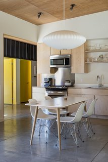 Plywood cabinetry and ceiling panels have been combined with white walls to create a clean kitchen setting. A Modernica Nelson Bubble Lamp hangs above the dining table.