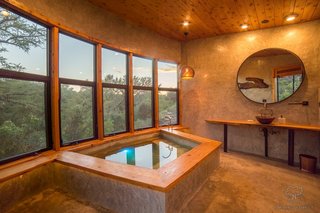 The custom concrete soaking tub is set in front of a wall of windows.