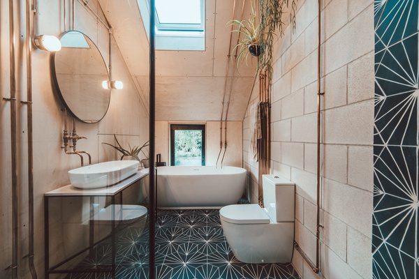 A peek inside the adjoining master bathroom decorated with Marrakesh Design wall tiles, air plants and exposed copper piping.