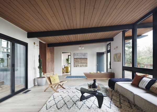 The updated living room features new wide-plank white oak hardwood floors. See Arch refinished the wood ceiling and structural beams, and stripped the walls of the original wood paneling for a brighter look.