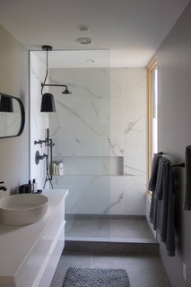 The guest bathroom boasts a minimalist look achieved with large, cement floor tiles and Statuario-style tiles on the walls.
