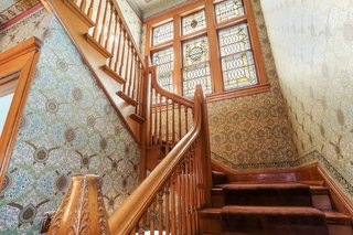 An original stained glass nine-panel window illuminates the stairway to the second floor. All wallpaper was created specifically for this home using architectural renderings for the design, and then hung by a Bradbury-licensed wallpaper artisan.
