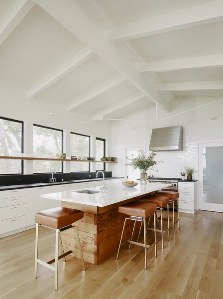 The expanded central kitchen occupies the heart of the home. The kitchen island is wrapped in reclaimed Douglas fir and topped with a white granite countertop. The countertops in the rear are black-flamed granite.