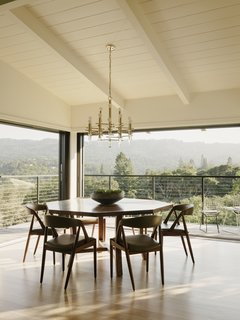 Surrounded by retractable glass doors, the dining area opens up to the landscape. A custom Gianni Corvasce Restoration walnut table is combined with vintage Kai Kristiansen dining chairs and a 1970s brass-and-Lucite chandelier.