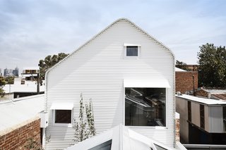 The architects designed an asymmetrical roof so as to avoid shading the neighbors' backyard. Note how the window awnings appear to peel up and away from the facade.