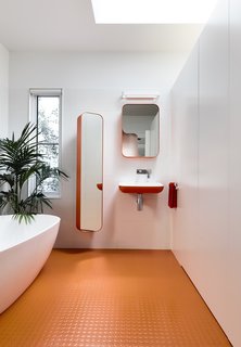 A skylight illuminates the master bathroom, which is entirely outfitted with Arblu Tulip fixtures. The orange floor is Kenbrock K2 studded rubber. Note how the divisional wall stops short of the ceiling—a decision that the architects implemented to “create volume and height, which celebrate the curve of the ceiling.”