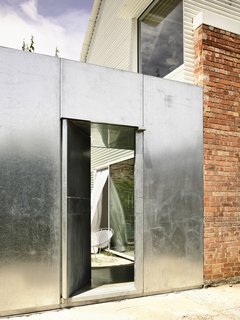 Built of galvanized steel, the new front door conveys safety and security. The owners had previously experienced a break-in, and they thought a more imposing entrance could serve as a deterrent. Directly behind the entry is the courtyard linking the old and new buildings.