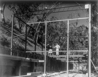 Ray and Charles Eames seen standing on the steel frame of the house, which consist of two rows of 4-inch H-columns set 20 feet apart. A 12-inch open-web joist forms the top member.