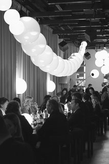 Design week guests dine under Opal pendant lamps arranged like a string of translucent pearls.