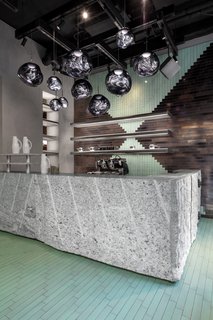 The entrance features a bar made from monolithic granite offcuts. The rough-cut granite is complemented by sleek lava stone tiles and Opal lights.