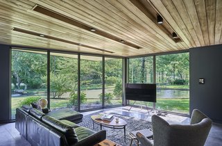 The "Man Cave," or lower lounge, opens up to the outdoors through full-height glazing. The chair and ottoman seen in the corner is by Modernica.