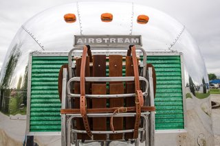 A redwood and teak folding rocking chair and loveseat are strapped to the back of Airstream with a bridle created by leatherworker Remco at Vanderhyde Toronto.