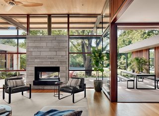 Walls of glass promote constant connection with the outdoors. The chairs that flank the double-sided fireplace are Kenmare armchairs by Modloft.