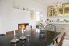 Modern home with Dining Room, Chair, Table, Stools, Ceiling Lighting, Light Hardwood Floor, Standard Layout Fireplace, Bar, Shelves, Accent Lighting, and Wood Burning Fireplace. Open dining room and kitchen featuring yellow stained glass cabinets, large black wooden table, and fireplace. Photo 7 of Colorful & Eclectic Danish Home