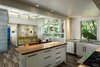 Modern home with Kitchen, Refrigerator, Dishwasher, Range, Range Hood, Granite Counter, Wood Counter, Pendant Lighting, Wood Cabinet, Porcelain Tile Floor, Ceiling Lighting, Drop In Sink, and Recessed Lighting. Main house kitchen, dining and front entrance that combines textures such as acid washed metals, wood, glass jalousie windows, and natural sunlight. Photo 4 of A Modern 1954 Plantation Style Home on Maui