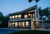 Modern home with Exterior, House Building Type, Metal Siding Material, Stucco Siding Material, and Flat RoofLine. Rear facade at dusk. Given the amazingly private rear yard, the house opens to the yard and welcomes reciprocal views. The warmth of the glow of interior lights spills out to the yard and patios. The client, being a mixed media artist, worked with artists to introduce a mural that held special personal meaning and importance. Photo 5 of Roslyn Road Residence