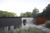 Modern home with Outdoor, Trees, Garden, Front Yard, Grass, and Walkways. Entrance view: An automated timber screen gives the entrance courtyard privacy from the street. Mature trees form a lush backdrop to the house with the front garden landscaped with chipped stone, grasses and aloes. Concrete storm water pies is placed as focal planters. Photo 6 of Grey House