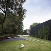 Modern home with Outdoor, Concrete Patio, Porch, Deck, Back Yard, Trees, Shrubs, Hardscapes, Grass, Stone Patio, Porch, Deck, Retaining Fences, Wall, Raised Planters, and Wood Fences, Wall. The backyard is a structured and geometric landscape. The fire pit doubles as a drainage pond for rainwater. Eventually, the ivy will completely hide the black stucco so one is surrounded by vegetation. Photo of The Winnwood Residence