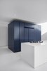 Modern home with Kitchen, Painted Wood Floor, Undermount Sink, Colorful Cabinet, Cooktops, Ceiling Lighting, and Refrigerator. A dark blue block is the central pole of the kitchen area. Deposited directly on the floor, its periphery creates a zone of circulation. Photo 4 of The House on Drolet Street