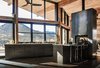 Modern home with Kitchen, Refrigerator, Microwave, Cooktops, Wood Cabinet, Dishwasher, Ceiling Lighting, Metal Cabinet, Dark Hardwood Floor, Concrete Floor, Concrete Counter, Range, Wall Oven, Pendant Lighting, Concrete Backsplashe, Accent Lighting, and Drop In Sink. The warm industrial kitchen celebrates views of Rocky Mountain National Park beyond. A see-through, steel fireplace becomes a glowing beacon that warms the kitchen and living room at the heart of the home. Photo 2 of Estes Park Residence