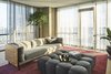 Modern home with Living Room, Ottomans, Sofa, Rug Floor, Ceiling Lighting, Floor Lighting, and Light Hardwood Floor. Living Room with wraparound balcony, cement walls, bubble tufted ottoman, wooden couch base, sheer curtains and red area rug. Photo 4 of Seaholm Custom Condo