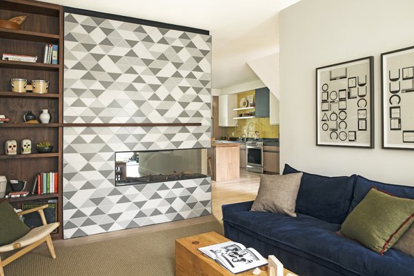 In a renovated California home, the double-sided fireplace anchors the first floor as a transitional element between entry, kitchen, dining room, and living room pictured. The fireplace tile was a custom designed shape by the interior designers and was manufactured locally by Fireclay Tile. The integrated bookcase and mantle were made by Kaimade Woodworking with locally sourced walnut.