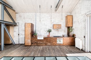 The kitchen area is full of charm, with cabinets made from reclaimed Iroko wood, incandescent lightbulb-style pendant lights hanging above the units, and a collection of potted house plants.