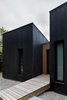 Modern home with Outdoor, Front Yard, Wood Patio, Porch, Deck, Trees, Wood Fences, Wall, Vertical Fences, Wall, Walkways, Woodland, and Decking Patio, Porch, Deck. The home's charred timber exterior resembles a crow's plumage. Photo 7 of La Binocle