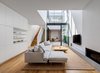 Modern home with Living Room, Sofa, Corner Fireplace, Coffee Tables, Ottomans, Medium Hardwood Floor, Gas Burning Fireplace, Bookcase, and Ceiling Lighting. Double height living area opens onto the home's interconnecting courtyard and floods the living space with natural light. Photo of Cloud House