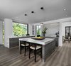 Modern home with Kitchen, Wood Cabinet, Cooktops, Ceiling Lighting, Drop In Sink, Refrigerator, Microwave, Light Hardwood Floor, Stone Slab Backsplashe, Dishwasher, Wall Oven, Pendant Lighting, and Engineered Quartz Counter. The owners goal with their Franklin homes kitchen, completed in 2017, was to emphasize the beautiful lake views and have a space that was open to a large family room and casual dining area. This contemporary kitchen combines convenience and function with hidden small appliances including a coffee station, toaster oven, microwave, to avoid cluttered countertops ensuring a clean look. The cooking area features an induction cooktop, mixer and a full quartz backsplash, as well as a hidden ventilation and lighting system in the soffit. A focal point is the large island which provides ample seating while leaving plenty of room for cooking and baking. Quartz was chosen for its beauty, durability, and ease of maintenance. The cabinetry features an integrated refrigerator, freezer, and dishwasher which complete the clean, uncluttered look. The kitchen also features two openings to the formal dining room providing easy flow and access for entertaining. Photo 10 of Contemporary Michigan Lake Home
