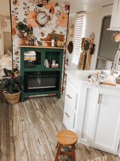 A floral partition cleverly disguises the master bedroom, providing a bit of privacy in this otherwise open space. A handsome green hutch rests in front of the partition, serving as multi-functional storage (mostly for kitchen items) as well as an electric fireplace.
