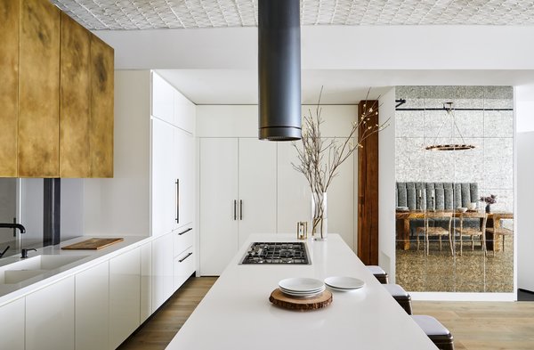 The distressed bronze upper cabinets and floating steel elements play off of the original tin ceilings and exposed timber columns of this historic cast iron SoHo loft building.