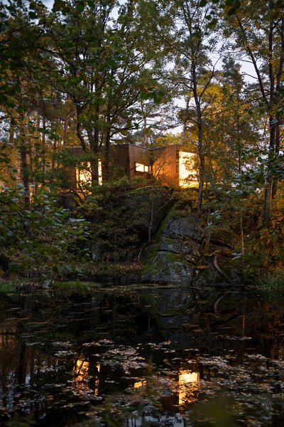 The cabin's large windows allow an unparalleled view of the pond it overlooks, while lush greenery seems to almost cover the exterior.