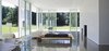 Modern home with Living Room, Ceiling Lighting, Table, Lamps, Coffee Tables, Accent Lighting, Wood Burning Fireplace, Ottomans, Track Lighting, Concrete Floor, Standard Layout Fireplace, Bench, and Sofa. The living room features twelve-foot by four-foot sheets of high-performance glass on the exterior of the main room are held in place with thermally broken sliding aluminum frames. These can be opened on temperate days, allowing the house to be cooled by cross breezes. Photo 2 of East Aurora Residence
