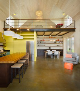 Situated underneath the loft, a cube comprising the refrigerator and pantry adds a dynamic, space-saving component to the kitchen.