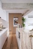 Modern home with Kitchen, Drop In Sink, Marble Counter, White Cabinet, Medium Hardwood Floor, Marble Backsplashe, Recessed Lighting, and Wood Cabinet. Open kitchen with a mixture of materials such as marble, wood, brass, and untouched concrete beams from the apartment's abandoned past, mixing the old and the new Photo 5 of Quarry Bay Residence