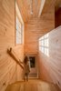 The wooden staircase of Tarusa House features a large street-facing window. Wood covers the floor, ceiling, and walls in most of this home designed by Architectural Bureau Project 905. Photo 16 of Tarusa House modern home