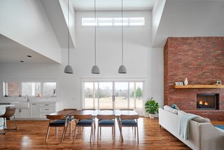The dining room of OKC Farmhouse by Scharbach Workshop features high ceilings, distinctive pendant lighting, and connects to the other areas of the house in an elegant way.