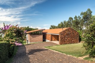 The view of the home from the driveway shows their staggered positions nestled into a slight slope. The materiality of the two volumes were an important element. The “private” structure on the right hosts the bedrooms and was constructed in stones pulled from the site, “adding a beautiful layer of the red colors from the region to the project.” The “social” structure on the left houses the communal living areas.