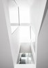 Modern home with Windows. View from the center of the ground floor looking up to the second floor and skylights below. Details on the ceiling above run perpendicular to the circulation above subtlety emphasizing the relationship at the stair and open to above. This architectural carve through both the exterior and interior volumes brings natural light into the center of the home. Photo 12 of Tesseract House