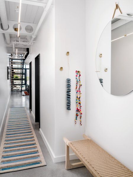 A simple, clean palette and double-duty lighting brighten up the entryway. Chioco selected a thin suspension light in brass from Juniper Lighting, a blue Scandinavian kilm runner from Black Sheep Unique, and a Danish bench from The Renner Project to cozy up the space.