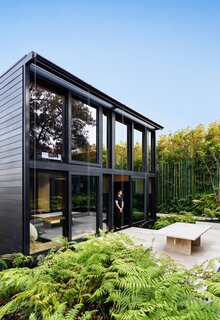 The rear curtain wall system opens to an outdoor patio raised above the tree-covered landscape.