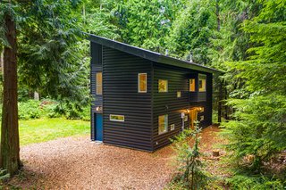 The two-level home rests on a lush property surrounded by 80-foot-tall trees. Simple black steel siding lends texture to the home’s facade.