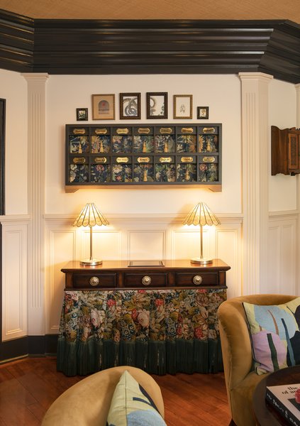 The custom key cabinet hangs above the vintage inlaid walnut check-in desk, which is wrapped in a handwoven jacquard fabric with silk fringe from Castel Maison.