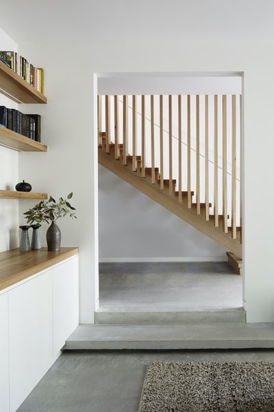 The lounge is accessed via two long concrete steps. On the stair opposite, the continuous vertical balustrade timbers extend to the ceiling of the second floor to form a sculptural element that allows natural light and ventilation to flow between the levels.