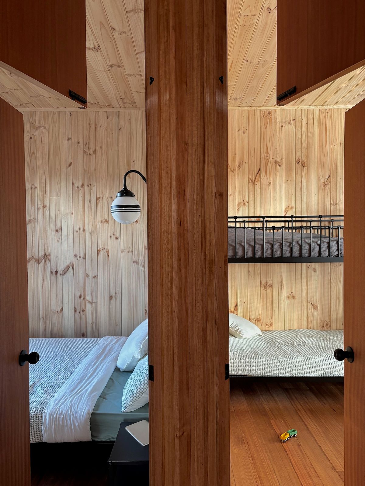 The floorplan prioritises simplicity, with the bedrooms located next to each other, each occupying a corner of the modest house. The wall-mounted lighting in the bedrooms and bathrooms echoes the pendant lighting used in the living areas, creating a sense of consistency.