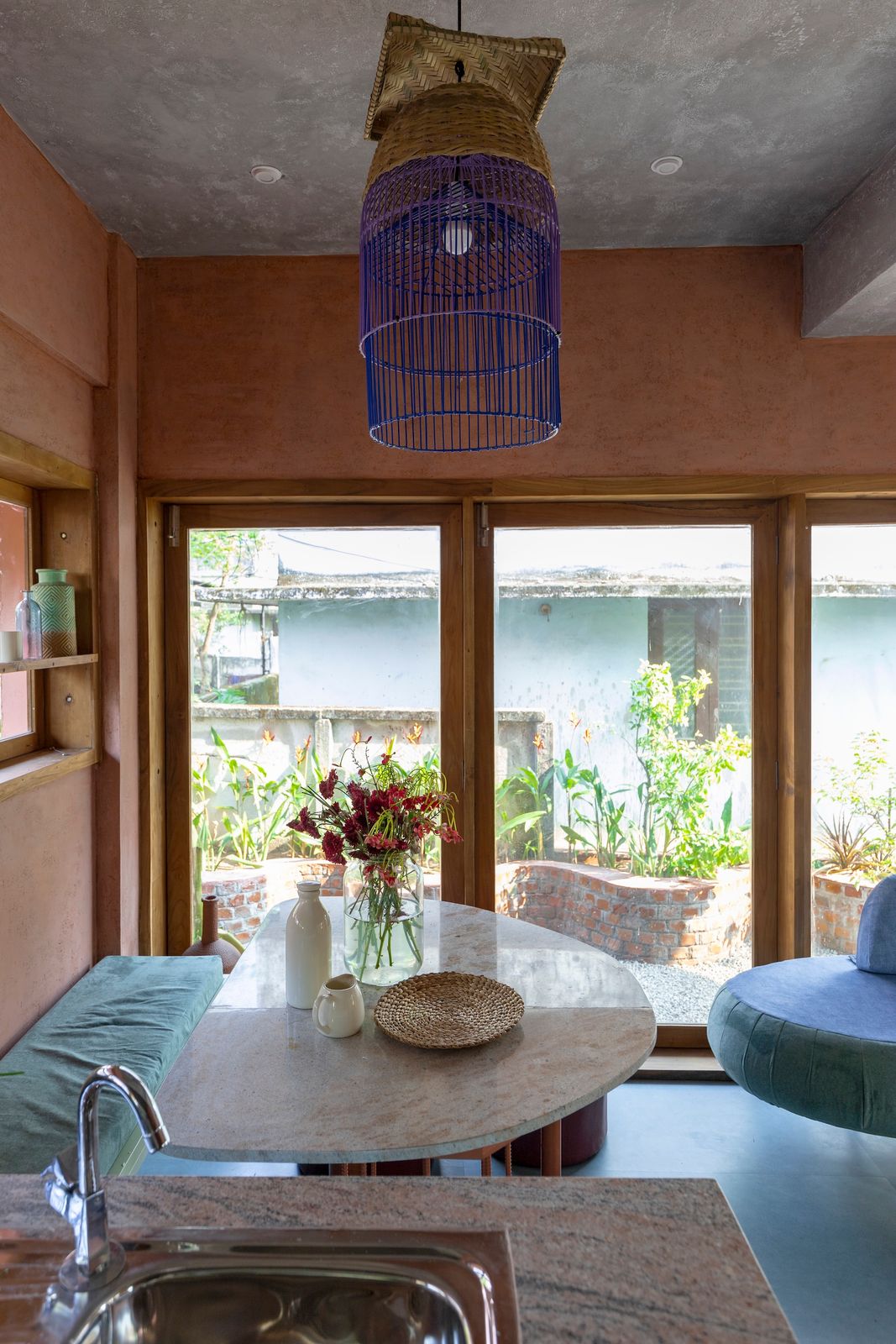 The pendant above the dining area is crafted from upcycled bird cages, painted blue to echo the color of the donated floor tiles used throughout the ground floor. The glass doors can be fully opened, extending the living area outside.